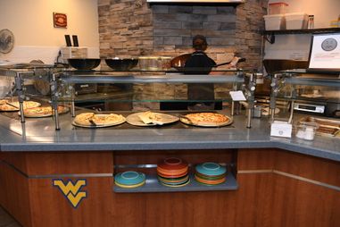 A WVU Dining Services employee places a pizza in the oven behind the counter at Summit Cafe