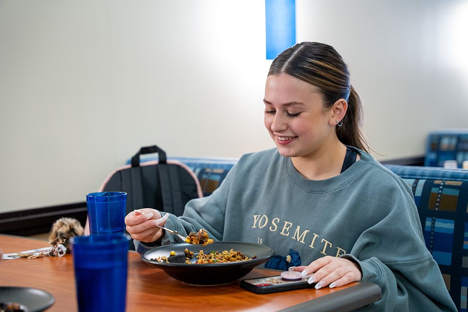 A student sits at a table in Cafe Evansdale enjoying a rice bowl from the Adobo Cantina station