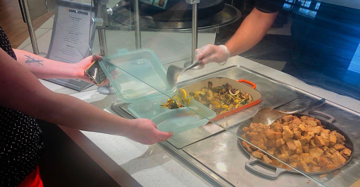 A Dining Services employee serves food in a to-go container