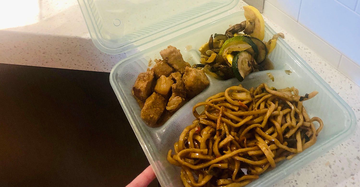 A to-go container is filled with noodles, chicken and sautéed vegetables 