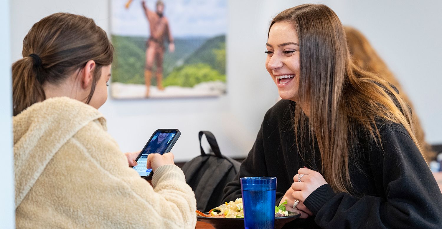 Two WVU students sit across from each other at Hatfields dining hall laughing and smiling